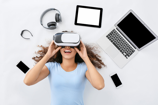 person laying on ground, surrounded by laptop, tablet and other technology